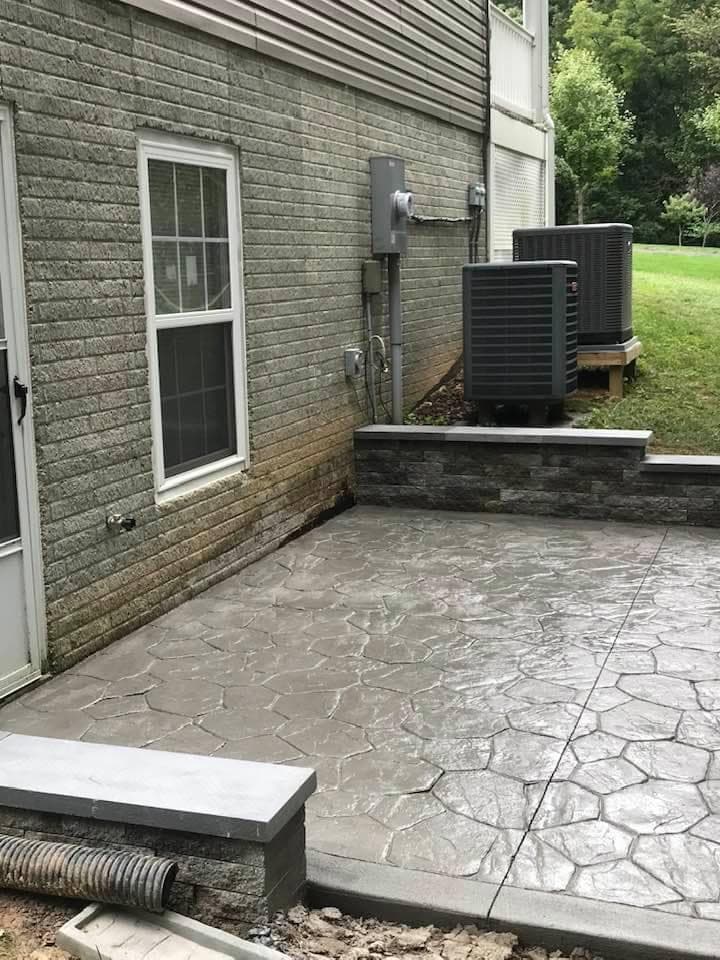 Flagstone-pattern concrete patio with stone seating wall behind a Maryland home